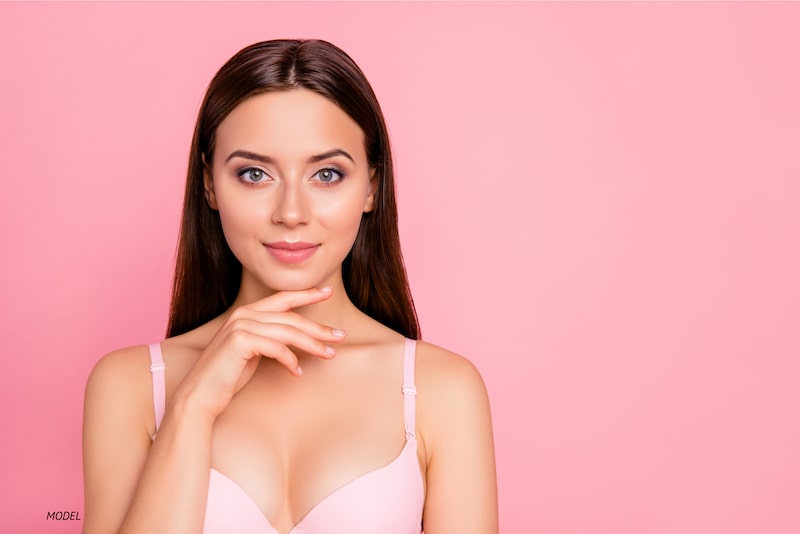Woman standing in pink bra against pink background.